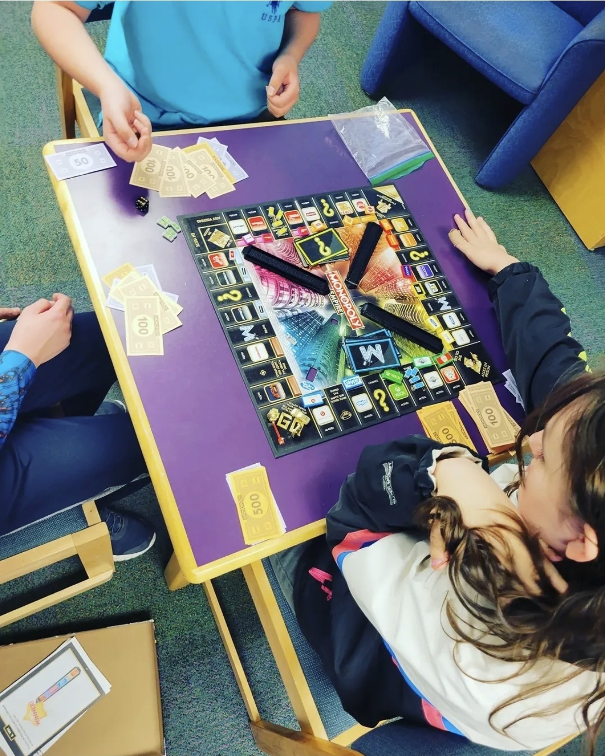Buddy UP! participants gathered around a Monopoly board on a purple table